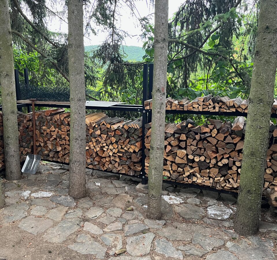 Dřevník pro palivové dřevo od drevnikovesteny.cz zakomponovaný v lesíku u domu